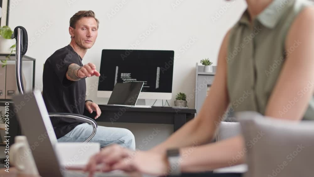 Medium slowmo of Caucasian programmer talking to female colleague typing program codes on laptop while working together on new software at home office Medium slowmo of Caucasian programmer talking to female colleague typing program codes on laptop while working together on new software at home office