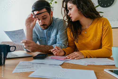 Serious Couple Paying Bills Together at Home. 
Worried man and woman talking about family budget and savings, calculating household bills and expenses while sitting at table with laptop and coffee.