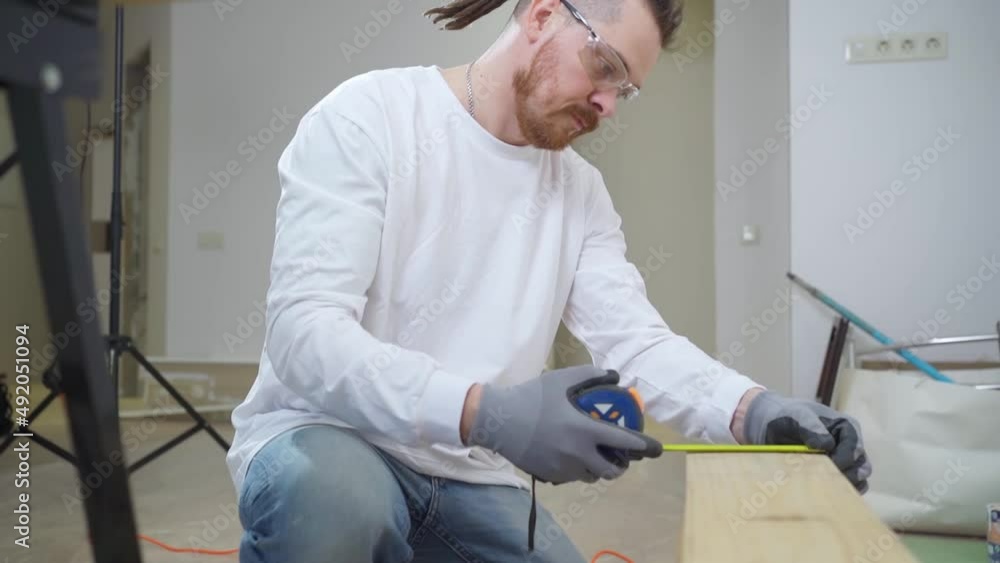 carpenter in protective gloves and glasses makes measurements on wood carpenter in protective gloves and glasses makes measurements on wood