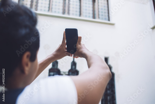Back view of young male tourist using cellphone device with mock up screen for clicking photos during international vacations, blurred man holding blank smartphone with copy space for travel website
