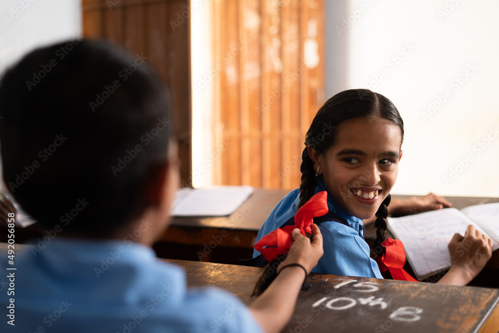 Boy from behind pulling ponytail of girl at classroom - conept of childhood crush, kids mischief, flirting and education Boy from behind pulling ponytail of girl at classroom - conept of childhood crush, kids mischief, flirting and education