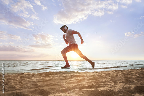sporty man running on a sandy beach at sunset .