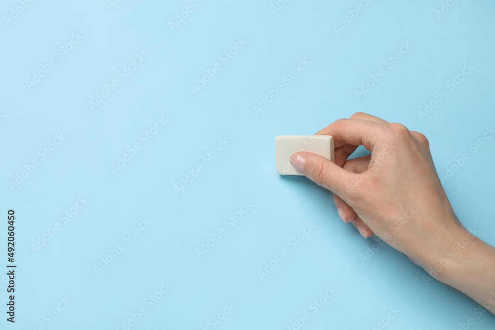 Woman erasing something on light blue background, closeup. Space for text Woman erasing something on light blue background, closeup. Space for text