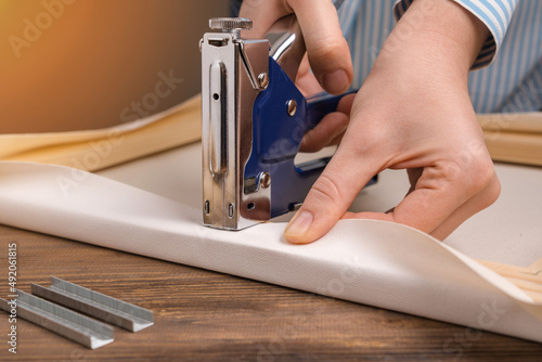 The artist stretches the canvas on a wooden frame with a stapler. Close-up, selective focus