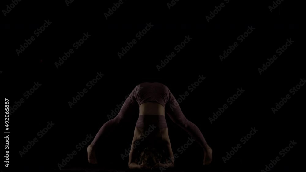 Fit woman practicing yoga poses. Silhouette girl doing exercise indoors against black background. No stress inner balance concept.. Fit woman practicing yoga poses. Silhouette girl doing exercise indoors against black background. No stress inner balance concept..