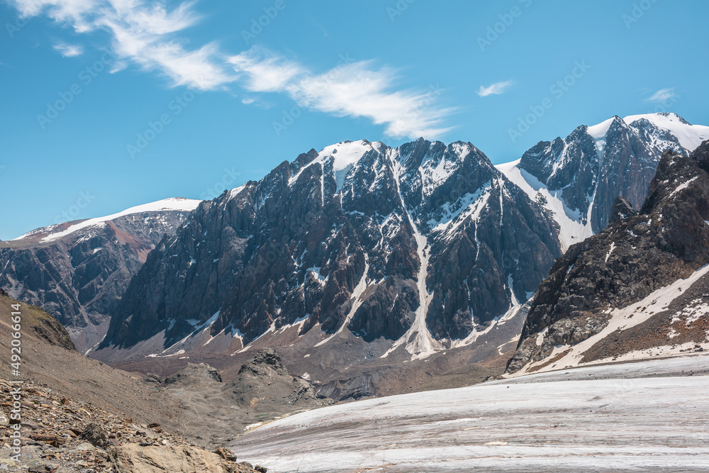 Scenic mountain landscape with glacier under sharp rocks in sunlight. Awesome landscape with glacial tongue and rocky pinnacle in sunshine. Beautiful view to snow mountains at very high altitude. Scenic mountain landscape with glacier under sharp rocks in sunlight. Awesome landscape with glacial tongue and rocky pinnacle in sunshine. Beautiful view to snow mountains at very high altitude.