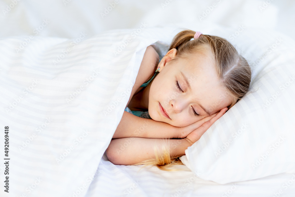 a girl child sleeps on a bed at home on a white cotton bed and smiles sweetly in her sleep with her hands folded under her cheeks a girl child sleeps on a bed at home on a white cotton bed and smiles sweetly in her sleep with her hands folded under her cheeks