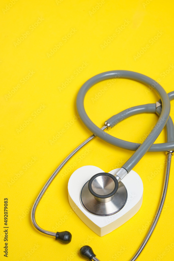 White heart and stethoscope on yellow background.Heart disease, medical examination.