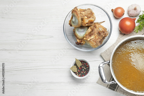 Delicious homemade bone broth and ingredients on white wooden table, flat lay. Space for text