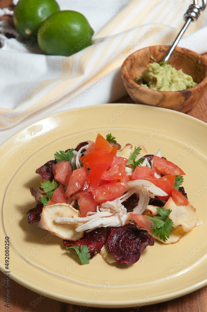 top view, medium distance of a yellow plate filled with beets and parsnip, chip nachos with shredded chicken and a bowl of guacamole top view, medium distance of a yellow plate filled with beets and parsnip, chip nachos with shredded chicken and a bowl of guacamole