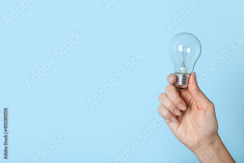Woman holding incandescent light bulb on blue background, closeup. Space for text