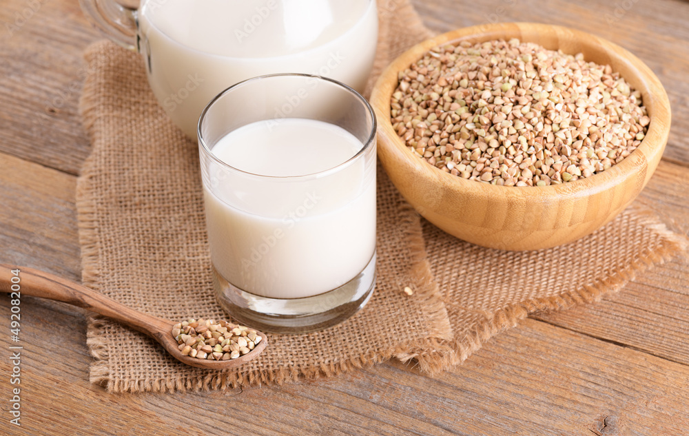 Vegan non diary buckwheat milk in glass with buckwheat groats and wooden spoon on a wooden background. Vegan buckwheat drink is plant based alternative milk . Veggies healthy milk product, copy space Vegan non diary buckwheat milk in glass with buckwheat groats and wooden spoon on a wooden background. Vegan buckwheat drink is plant based alternative milk . Veggies healthy milk product, copy space