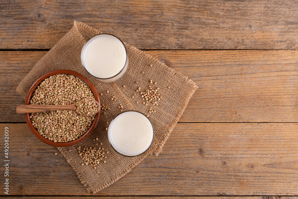 Vegan non diary buckwheat milk in glasses with buckwheat groats in a clay bowl on a wooden background. Vegan buckwheat drink is plant based alternative milk . Veggies healthy milk product, copy space Vegan non diary buckwheat milk in glasses with buckwheat groats in a clay bowl on a wooden background. Vegan buckwheat drink is plant based alternative milk . Veggies healthy milk product, copy space