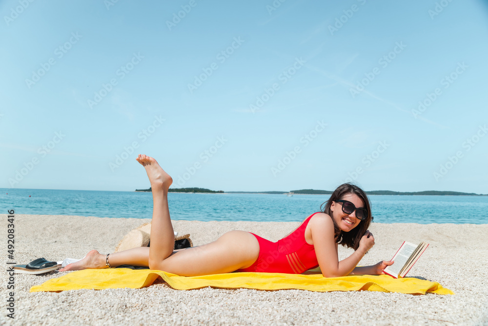 young sexy stunning woman in red swimsuit reading book on sea beach