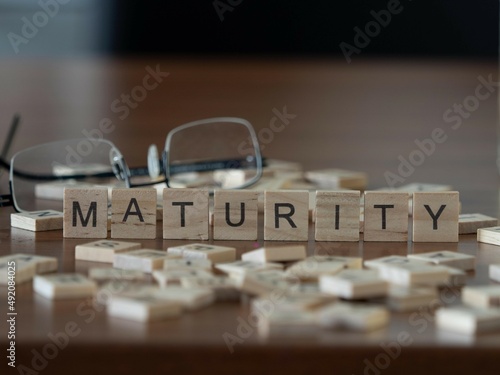 maturity word or concept represented by wooden letter tiles on a wooden table with glasses and a book photo