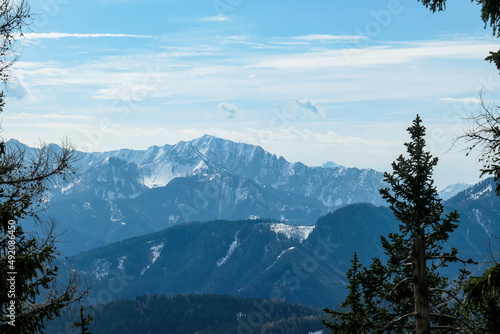 Scenic view of snow capped mountain peaks of Karawanks on the way to Sinacher Gupf in Carinthia, Austria. Mount Loibler Baba is visible through dense forest in early spring. Rosental on a sunny day