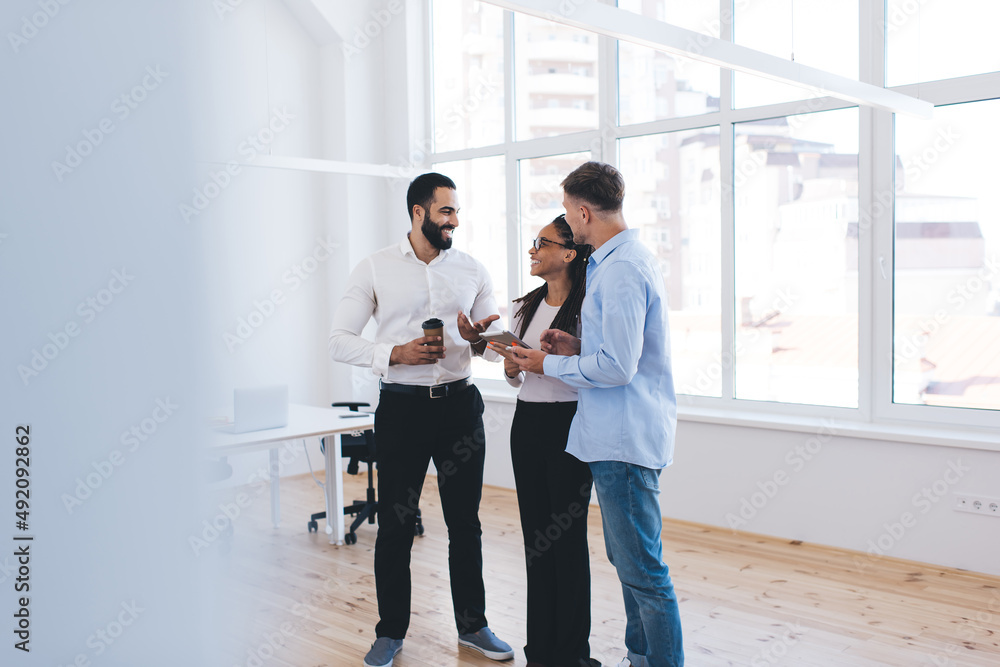 Fototapeta premium Diverse male and female colleagues in smart casual clothes discussing digital tablet options during office conversation about together brainstorming, successful partners talking during coffee break