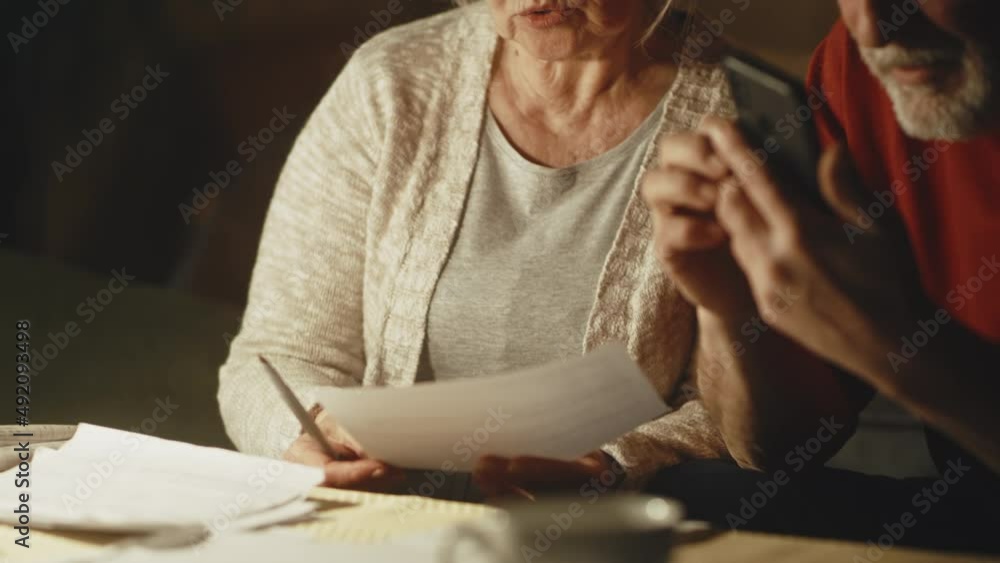 View of senior man with smartphone making calculations while discussing utility bills with wife in evening at home View of senior man with smartphone making calculations while discussing utility bills with wife in evening at home