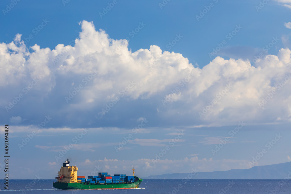 cargo ship nearby Capo Peloro Lighthouse in Punta del Faro on the Strait of Messina, most north eastern promontory of Sicily, Italy