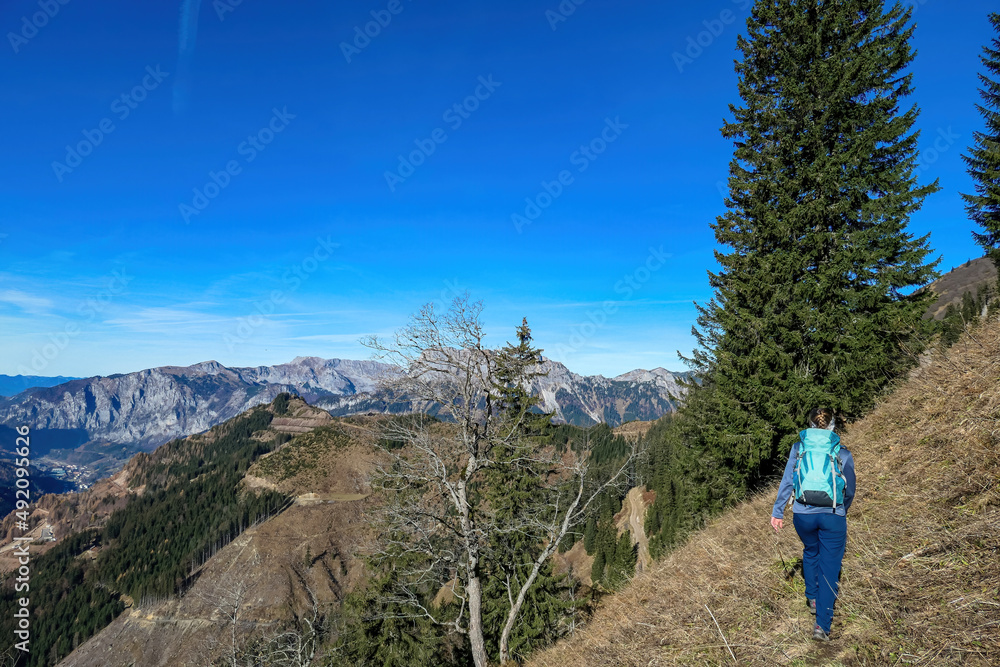 Happy woman with a backpack on a scenic hiking trail leading to mount Eisenerzer Reichenstein in Styria, Austria, Europe. Austrian Ennstal Alps. Alpine meadows in autumn season. View on Kaiserschild