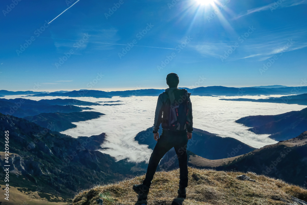 A man enjoying the panoramic view from mount Eisenerzer Reichenstein in Styria, Austria, Europe. The Ennstal valley is covered in clouds and fog.Hiking trail,Wanderlust. Sunny day.Freedom concept