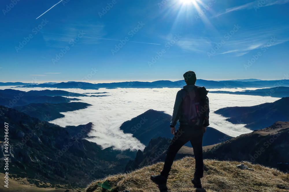 A man enjoying the panoramic view from mount Eisenerzer Reichenstein in Styria, Austria, Europe. The Ennstal valley is covered in clouds and fog.Hiking trail,Wanderlust. Sunny day.Freedom concept