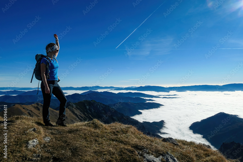 Woman with backpack hiking and admiring a scenic view from mount Eisenerzer Reichenstein in Styria, Austria, Europe. Ennstal valley is covered in clouds. Hiking trail, Wanderlust. Freedom concept