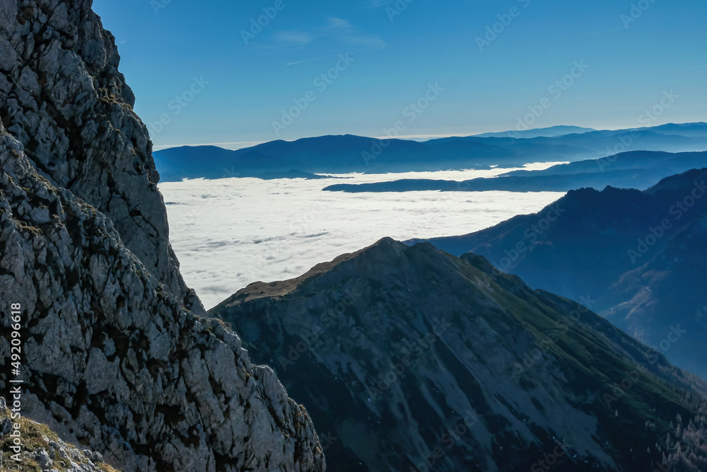 Obraz premium A massive cliff of mount Eisenerzer Reichenstein in Styria, Austria, Europe. Austrian Alps. Bare mountain ridges with view on the cloud covered Ennstal Valley. Hiking trail, Wanderlust. Sunny day