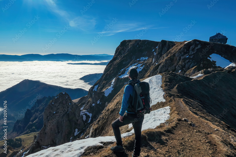 A man enjoying the panoramic view from mount Eisenerzer Reichenstein in Styria, Austria, Europe. Ennstal valley is covered in clouds and fog. Hiking trail to cottage. Sunny day. Freedom concept