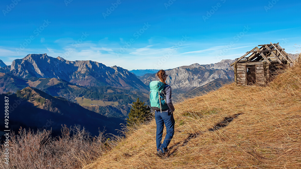 A woman in front of an abandoned and destroyed cottage enjoying the panoramic view near mount Eisenerzer Reichenstein in Styria, Austria, Europe. Hiking trail, Wanderlust.Sunny day.Exploration concept