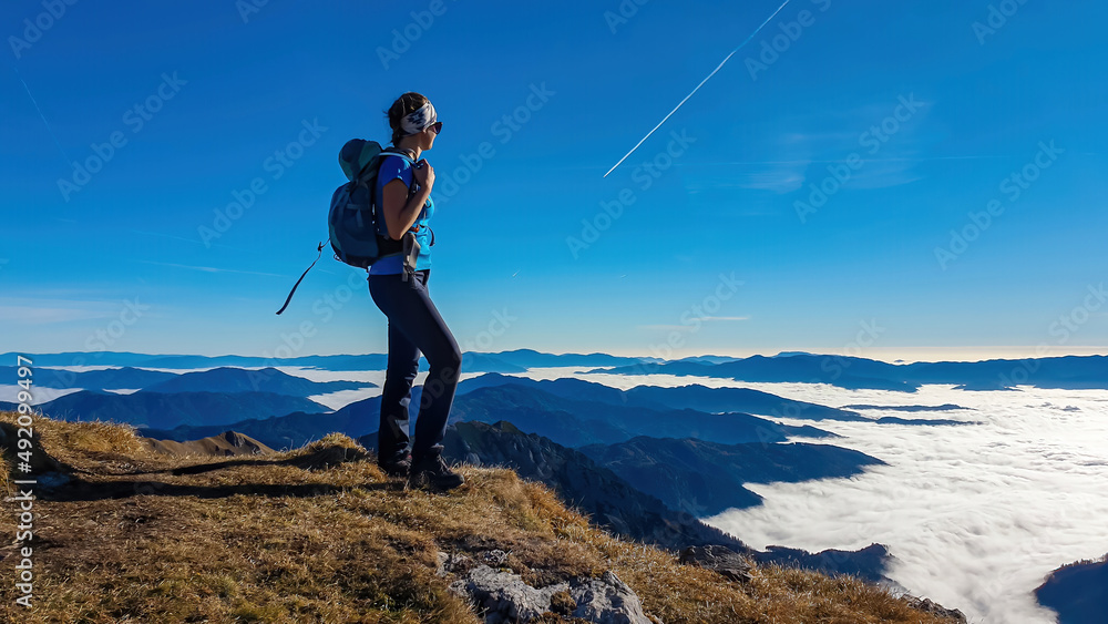 A woman enjoying the panoramic view from mount Eisenerzer Reichenstein in Styria, Austria, Europe. The Ennstal valley is covered in clouds and fog. Hiking trail, Wanderlust. Sunny day. Freedom concept A woman enjoying the panoramic view from mount Eisenerzer Reichenstein in Styria, Austria, Europe. The Ennstal valley is covered in clouds and fog. Hiking trail, Wanderlust. Sunny day. Freedom concept