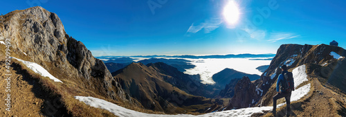 A man enjoying the panoramic view from mount Eisenerzer Reichenstein in Styria, Austria, Europe. The Ennstal valley is covered in clouds and fog.Hiking trail,Wanderlust. Sunny day.Freedom concept photo