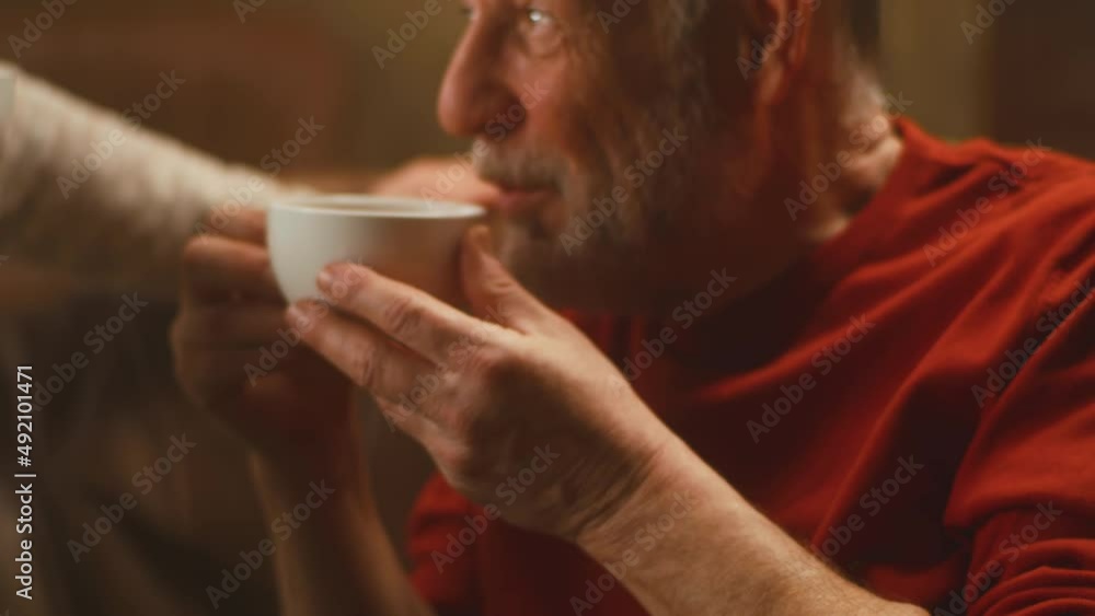 View of aged husband and wife enjoying fresh tea and speaking with each other while resting on sofa in weekend at home View of aged husband and wife enjoying fresh tea and speaking with each other while resting on sofa in weekend at home