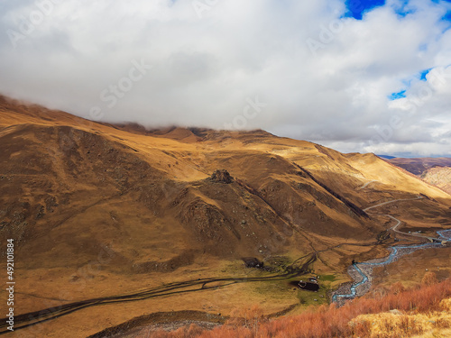 The clouds descended on the tops of the Caucasian mountains in the gorge of which a winding river flows and traces of passing cars are visible. Autumn in the Jily-su valley
