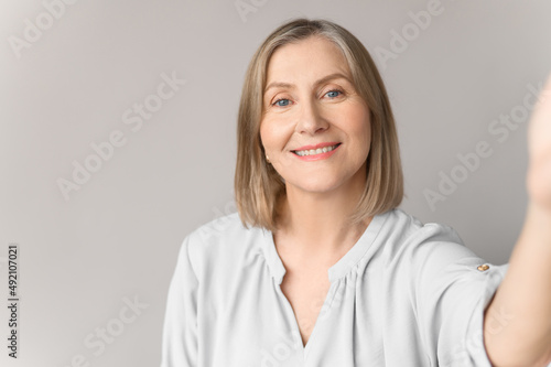 Close up self-portrait picture of smiling old woman on light background. Charmind age lady make selfie.