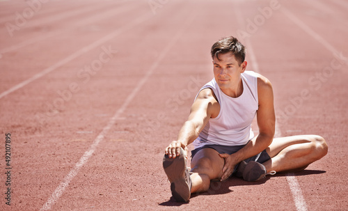 Preparing to win. Shot of an athlete stretching his legs while sitting on the track.