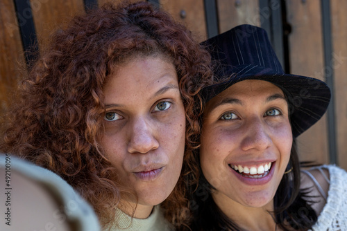 Two adult Latin American women (34 and 29), both with green eyes and positive attitude have fun taking a self-portrait while making gestures with their faces. Lifestyle and technology concept.