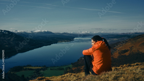 woman sat on the top of a mountain overlooking a loch