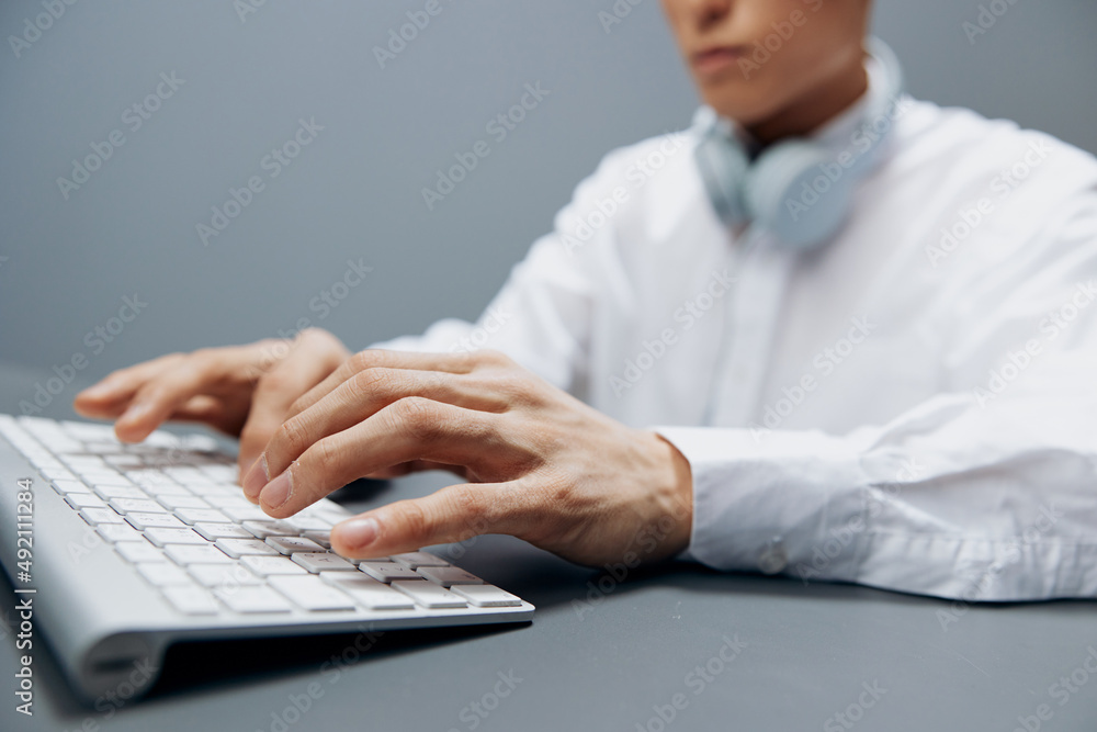 man in headphones hands on keyboard office work close-up Gray background man in headphones hands on keyboard office work close-up Gray background