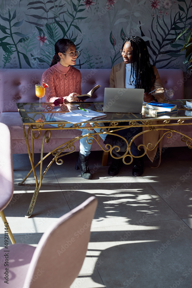 Two multicultural female students sitting in cafeteria and study for exam. Two multicultural female students sitting in cafeteria and study for exam.