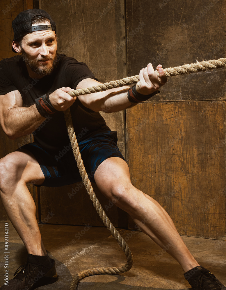 Caucasian strong man pulling rope, cross training gym Stock Photo