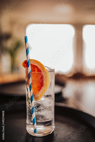 A close up shot of a glass with gin tonic, slice of a grapefruit and blue paper straw inside. Refreshing summer cocktail drink. Concept of hospitality, bars and restaurants. photo