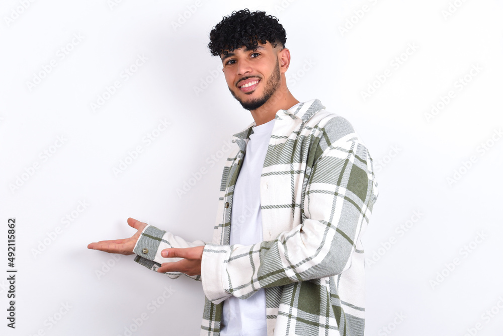 young arab man with curly hair wearing overshirt over white background Inviting to enter smiling natural with open hands. Welcome sign. young arab man with curly hair wearing overshirt over white background Inviting to enter smiling natural with open hands. Welcome sign.