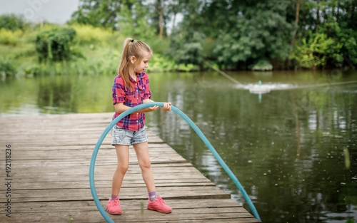 A blonde girl stands on a wooden pier on the river bank.