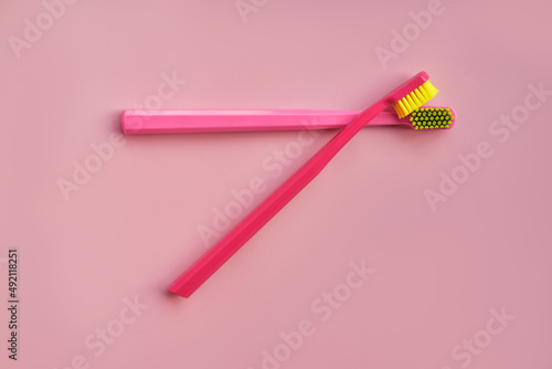Two pink toothbrushes stand in pink glass on pink background. One brush is new and other has been used. Yellow bristles are disheveled  green bristles are new.