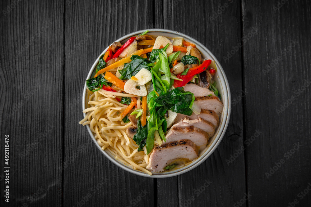 Soba Noodles in broth with chicken fillet, vegetables: carrots, sweet peppers, broccoli on a black background. Sushi menu. Japanese food Soba Noodles in broth with chicken fillet, vegetables: carrots, sweet peppers, broccoli on a black background. Sushi menu. Japanese food