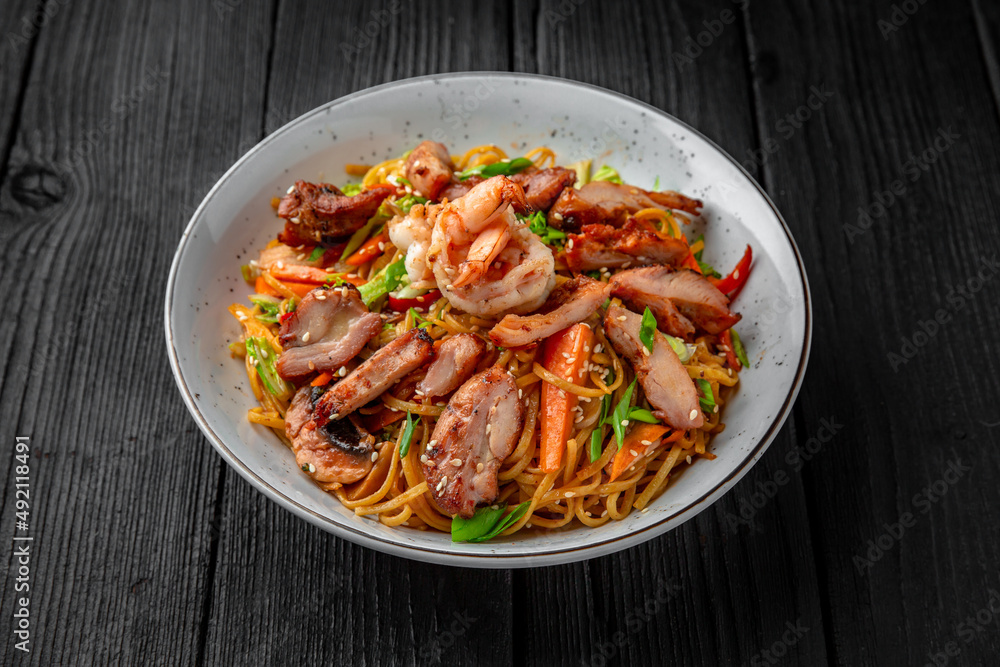 Soba Noodles with chicken, shrimp, mushrooms and vegetables: carrots, sweet peppers, broccoli on a black background. Sushi menu. Japanese food Soba Noodles with chicken, shrimp, mushrooms and vegetables: carrots, sweet peppers, broccoli on a black background. Sushi menu. Japanese food