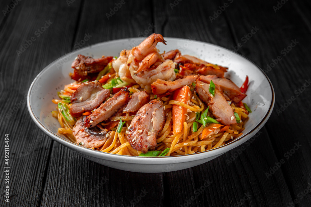 Soba Noodles with chicken, shrimp, mushrooms and vegetables: carrots, sweet peppers, broccoli on a black background. Sushi menu. Japanese food Soba Noodles with chicken, shrimp, mushrooms and vegetables: carrots, sweet peppers, broccoli on a black background. Sushi menu. Japanese food