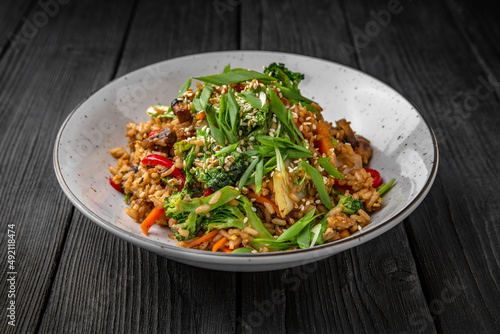 A plate of delicious rice with mushrooms and vegetables: carrots, sweet peppers, greens, spices and sauce on a black background