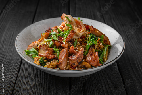 A plate of delicious rice with beef, shrimp and vegetables: carrots, sweet peppers, greens, spices and sauce on a black background
